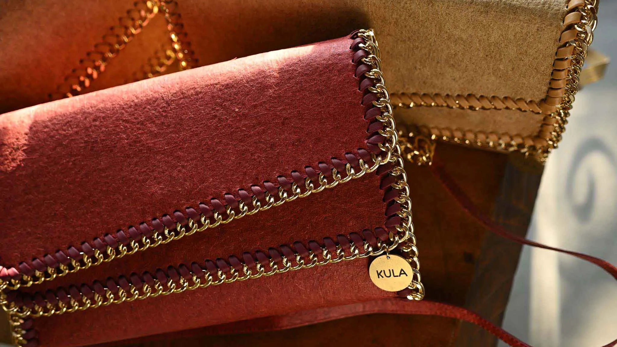 Bella handbags in terracotta red with morning light shining on the brand's gold tone circular metal badge.