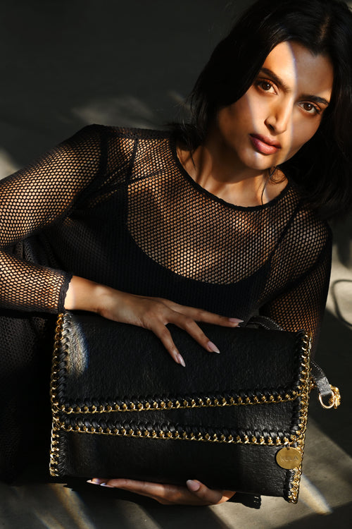 Female model holding a charcoal black bella handbag with gold accents against a dark background