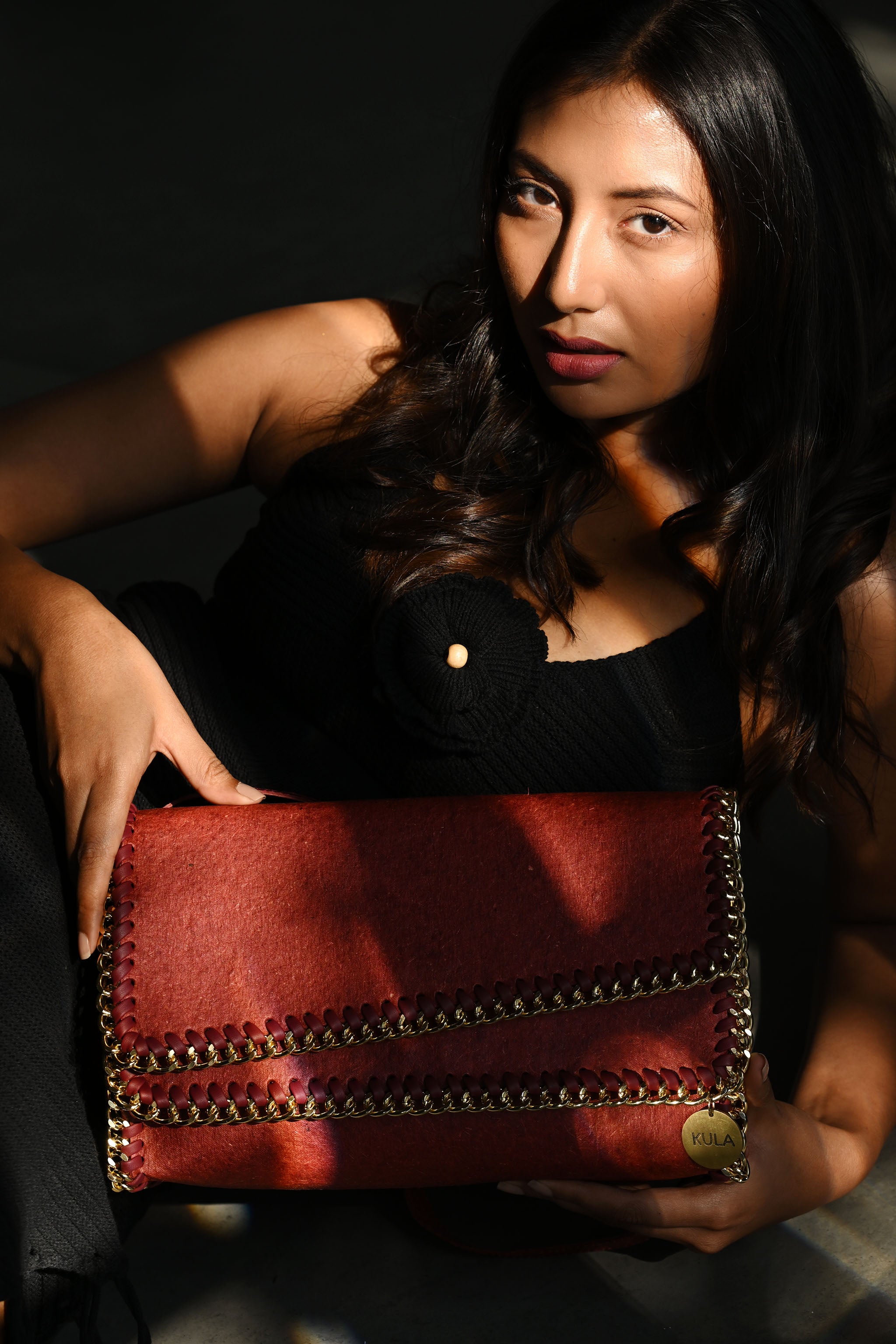 Female model holding a terracotta red bella handbag with a dark background